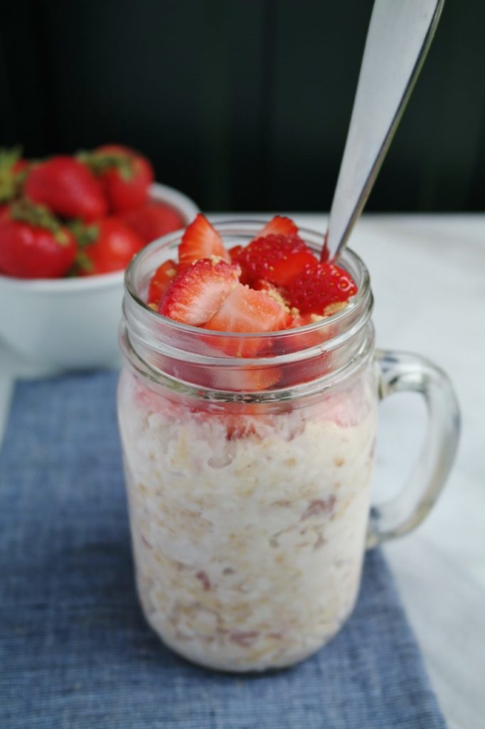 overnight strawberry cheesecake oats in a glass jar with fresh strawberries